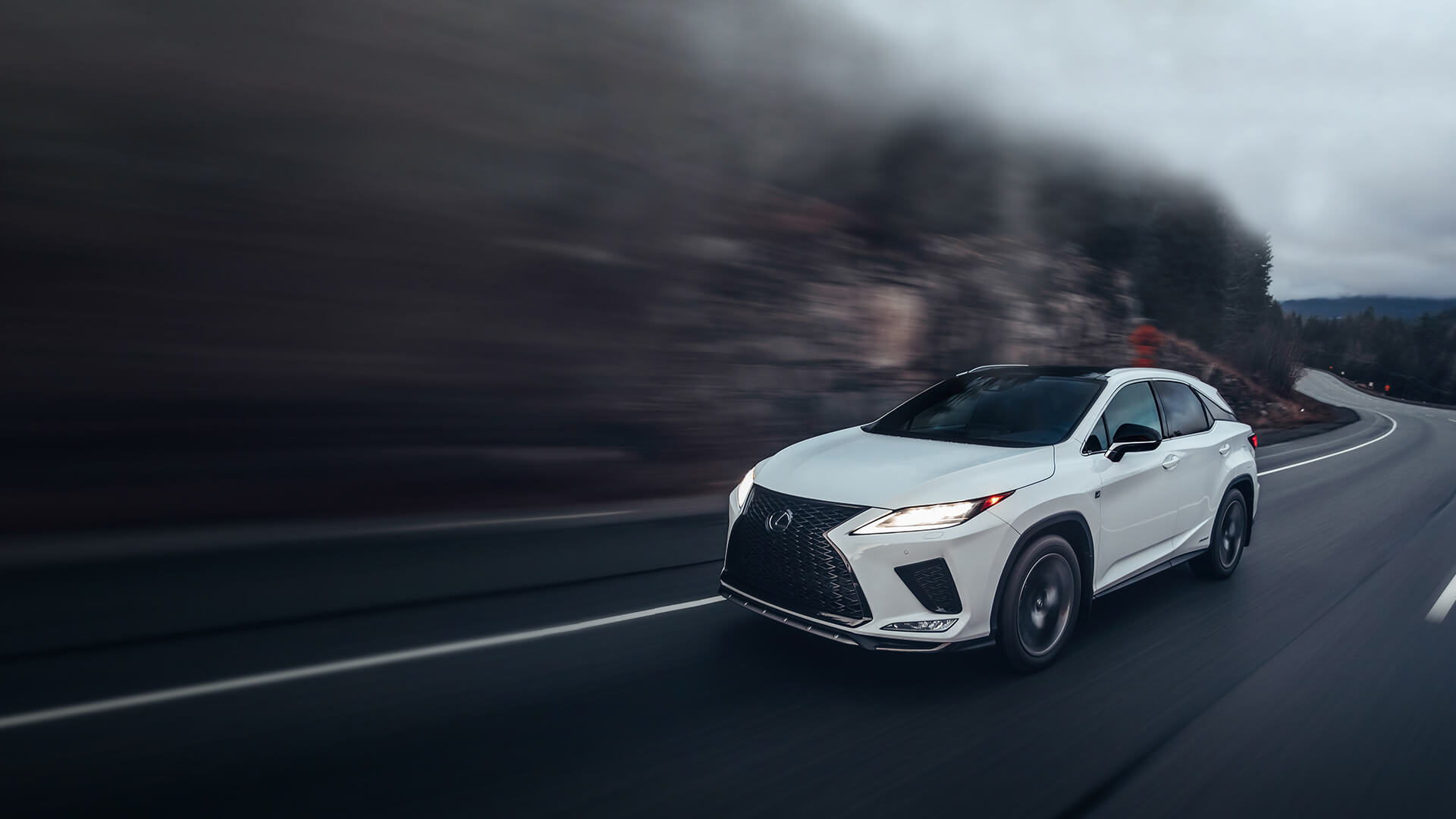 White Lexus RX being driven on the road with a mountainous backdrop.